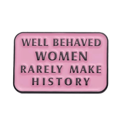 A rectangular pink sign with black raised letters stating WELL BEHAVED WOMEN RARELY MAKE HISTORY, inspired by the iconic enamel pin and badge.