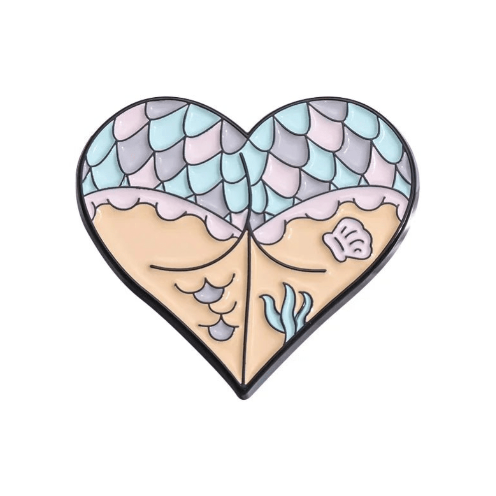 Heart-shaped enamel pin features pastel mermaid scales, skeleton hands holding a sandy beach and shell, plus seaweed accents for a gothic touch.