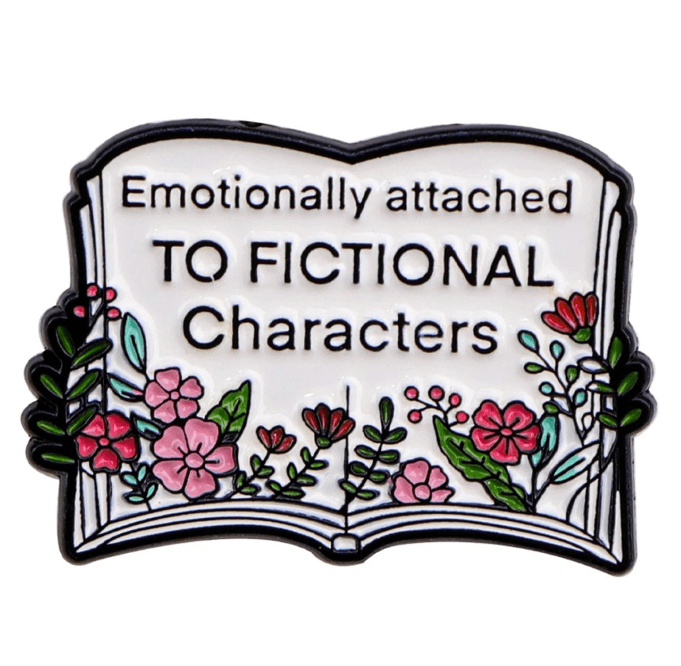 Enamel pin features an open book with colorful flowers and a charming book stack, plus the phrase “Emotionally attached to fictional characters” on its pages.