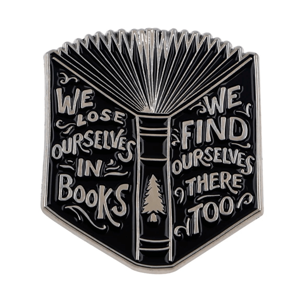 A metal pin shaped like an open book, engraved with We lose ourselves in books, we find ourselves there too—a stylish accessory for any Booktrovert.