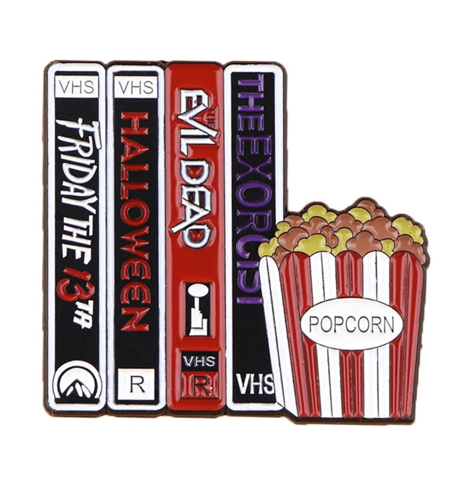 Enamel pin showcases VHS tapes of Friday the 13th, Halloween, The Evil Dead, and The Exorcist beside a red-and-white popcorn container labeled Popcorn—ideal for film buffs and badge collectors.