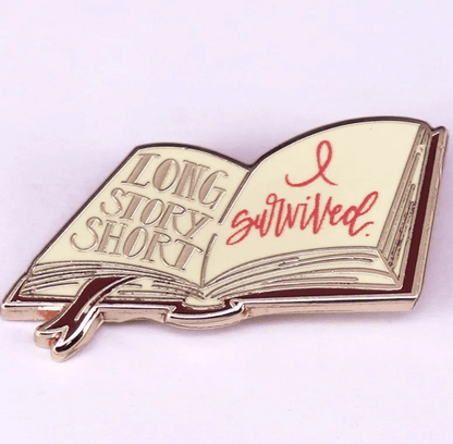 Enamel pin is shaped like an open book, with LONG STORY SHORT and I survived. in red cursive, plus a ribbon bookmark—an ideal badge for romance readers or book lovers.