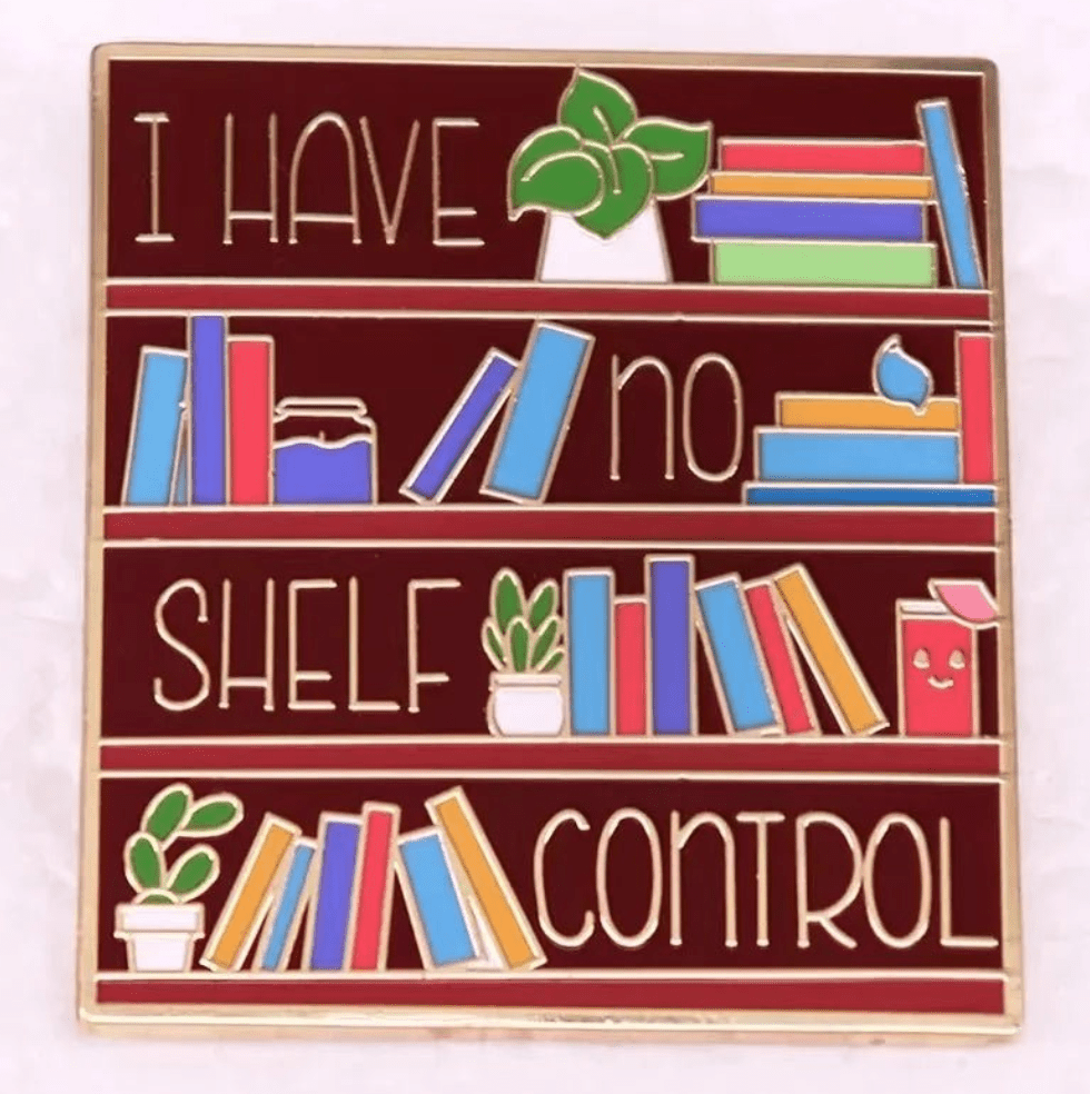 Kiss Me Later’s enamel pin for book lovers features three bookshelves with books and plants spelling I have no shelf control on a dark red background—perfect for any romance reader.