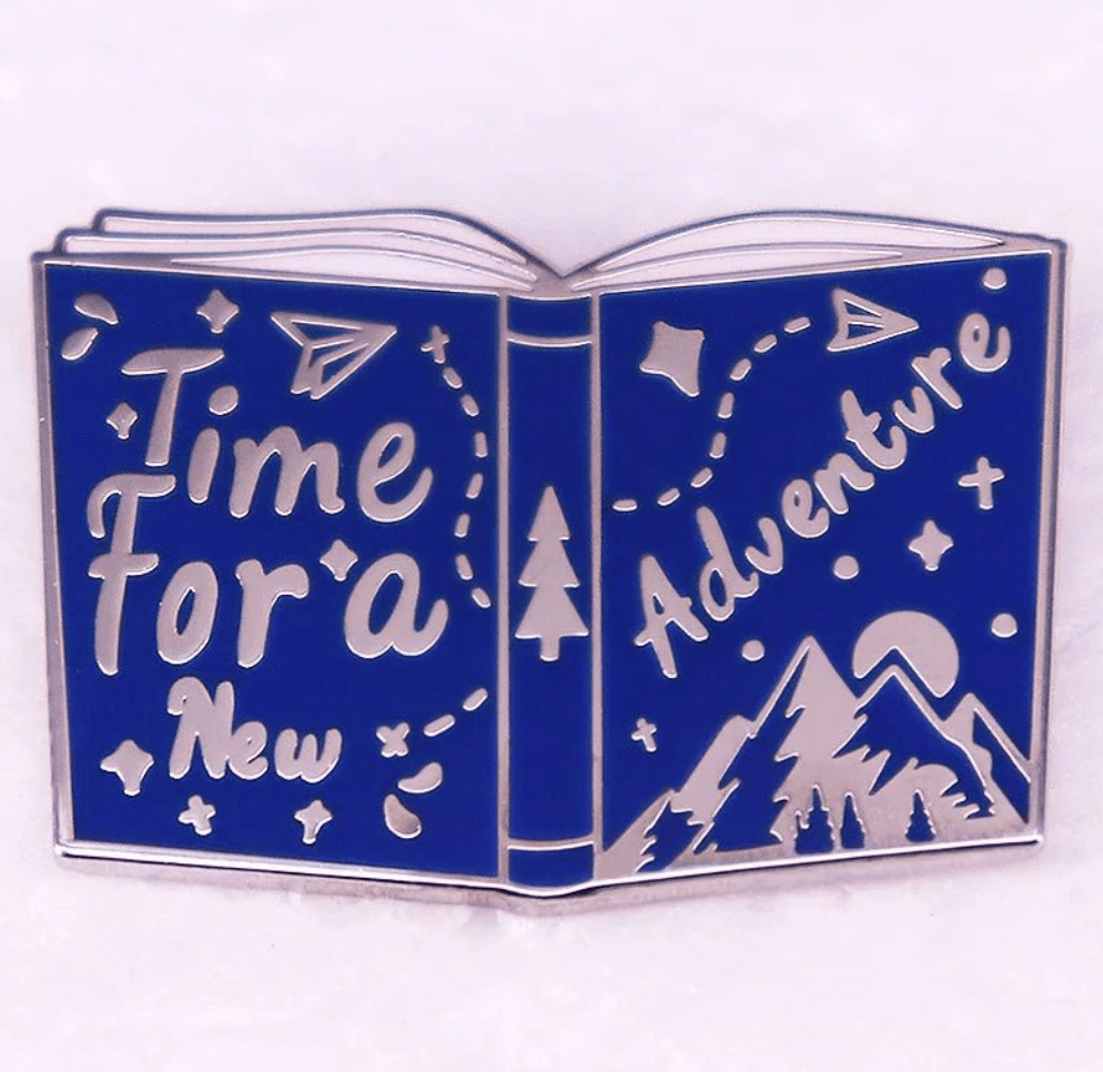 A Kiss Me Later enamel pin shaped like an open book with Time for a New Adventure, featuring mountains and stars—ideal for Romance Reader fans and book lover badge collectors.