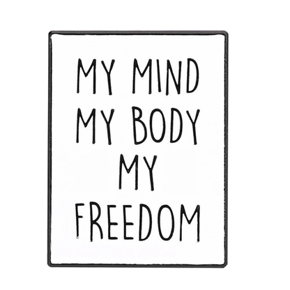 A white sign with bold, black capital letters reads: MY MIND MY BODY MY FREEDOM. The centered text is framed by a thin black border, echoing the empowering statement  feminist pins.