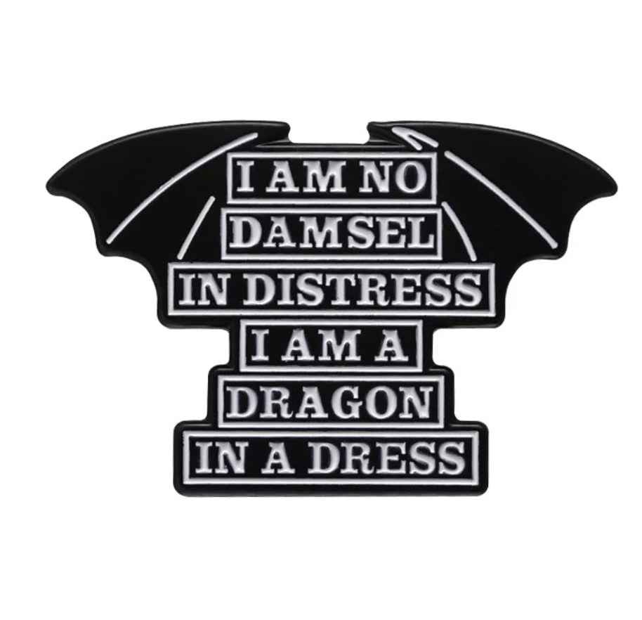Black enamel bat wing pin features white text: I am no damsel in distress, I am a dragon in a dress—a bold feminist accessory for your collection.