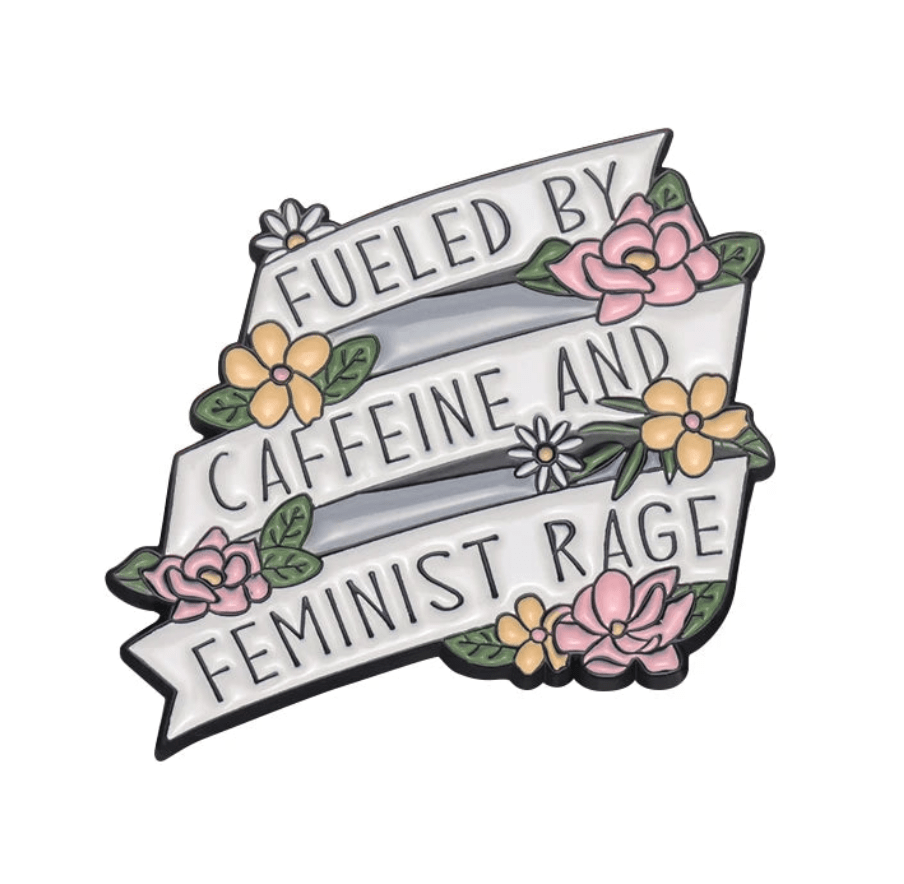 A decorative enamel pin features three white banners with black Fueled by caffeine and feminist rage text, accented with pink/yellow flowers and green leaves—perfect for fans of bold feminist accessories.
