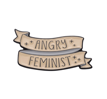A beige enamel pin features bold black ANGRY FEMINIST lettering outlined in black and surrounded by small stars—a standout addition to any feminist pin collection.