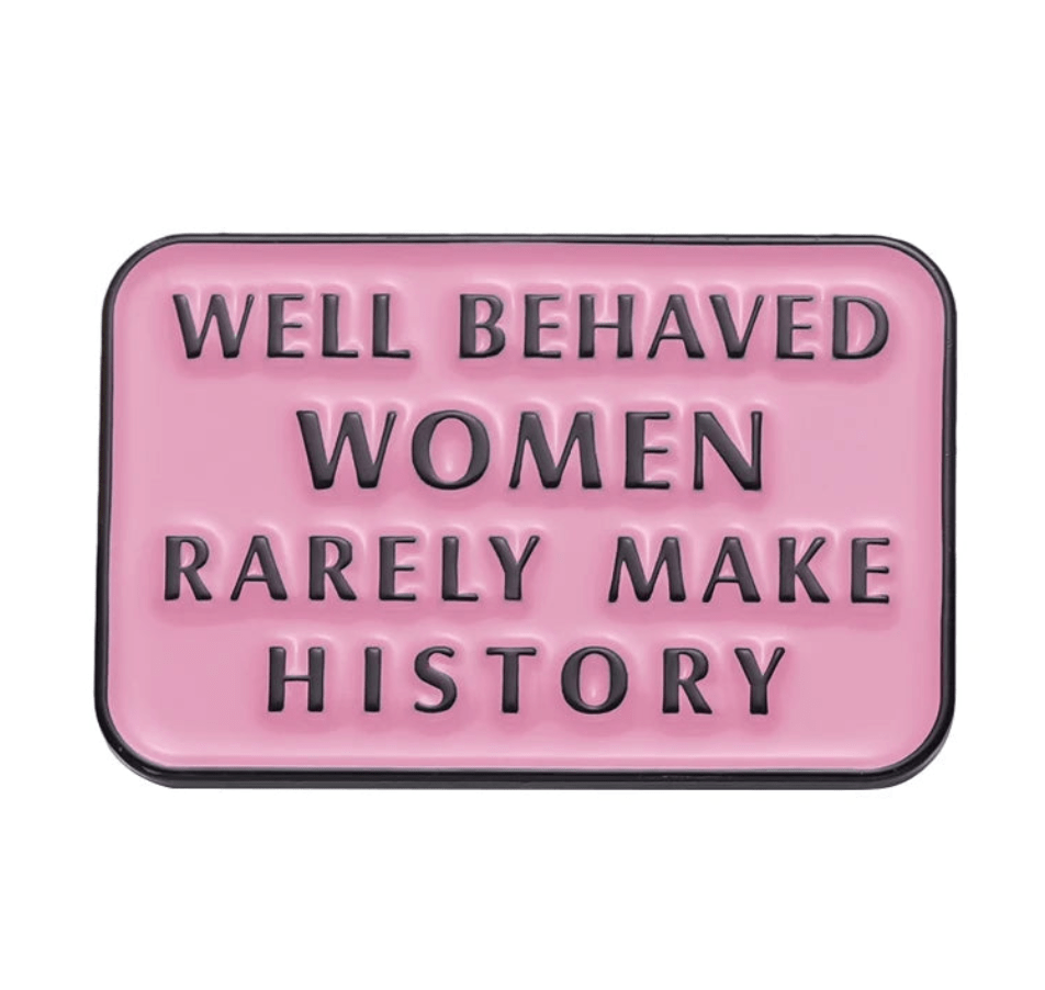 A pink rectangular enamel pin featuring bold black text: WELL BEHAVED WOMEN RARELY MAKE HISTORY—a standout feminist accessory for any collection.