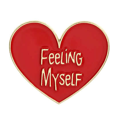 Heart-shaped enamel pin features elegant gold edges and gleaming gold words Feeling Myself across its red and gold design.