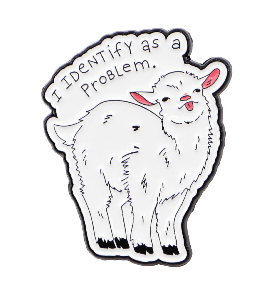 A cute illustrated goat stands smiling, wearing a red love heart enamel pin, with I identify as a problem written above. 