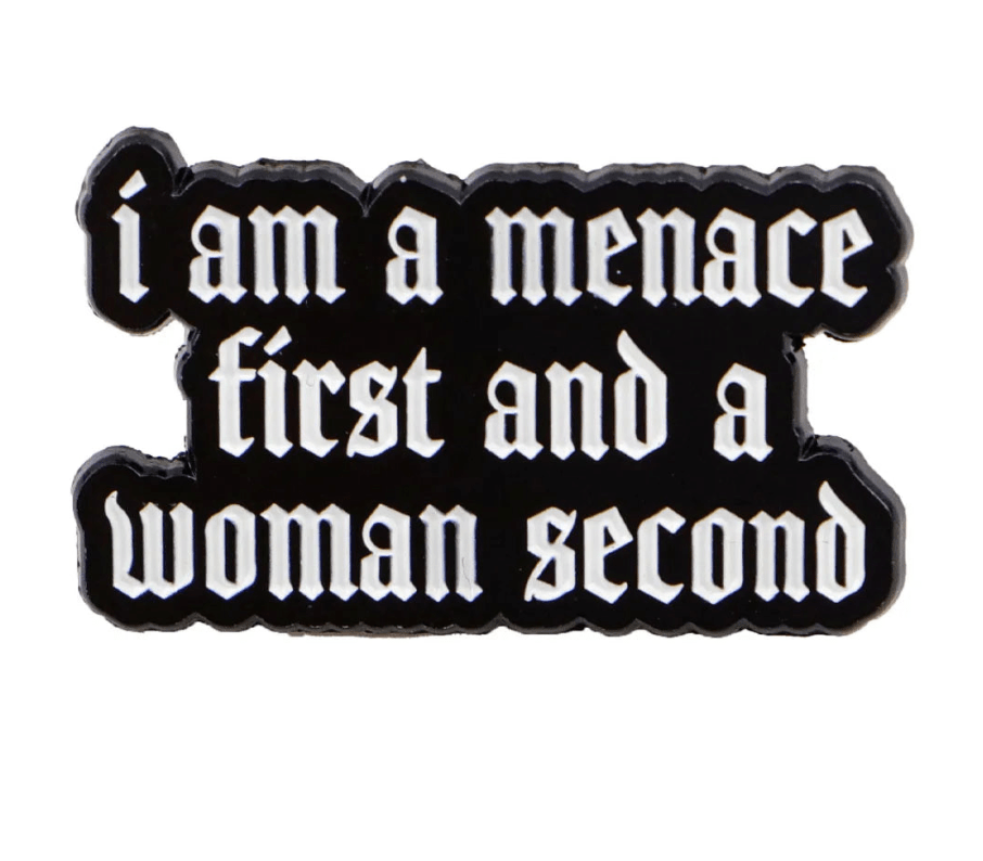 black pin features white Gothic script reading i am a menace first and a woman second, making it the perfect edgy companion to your favorite red love heart enamel pin.