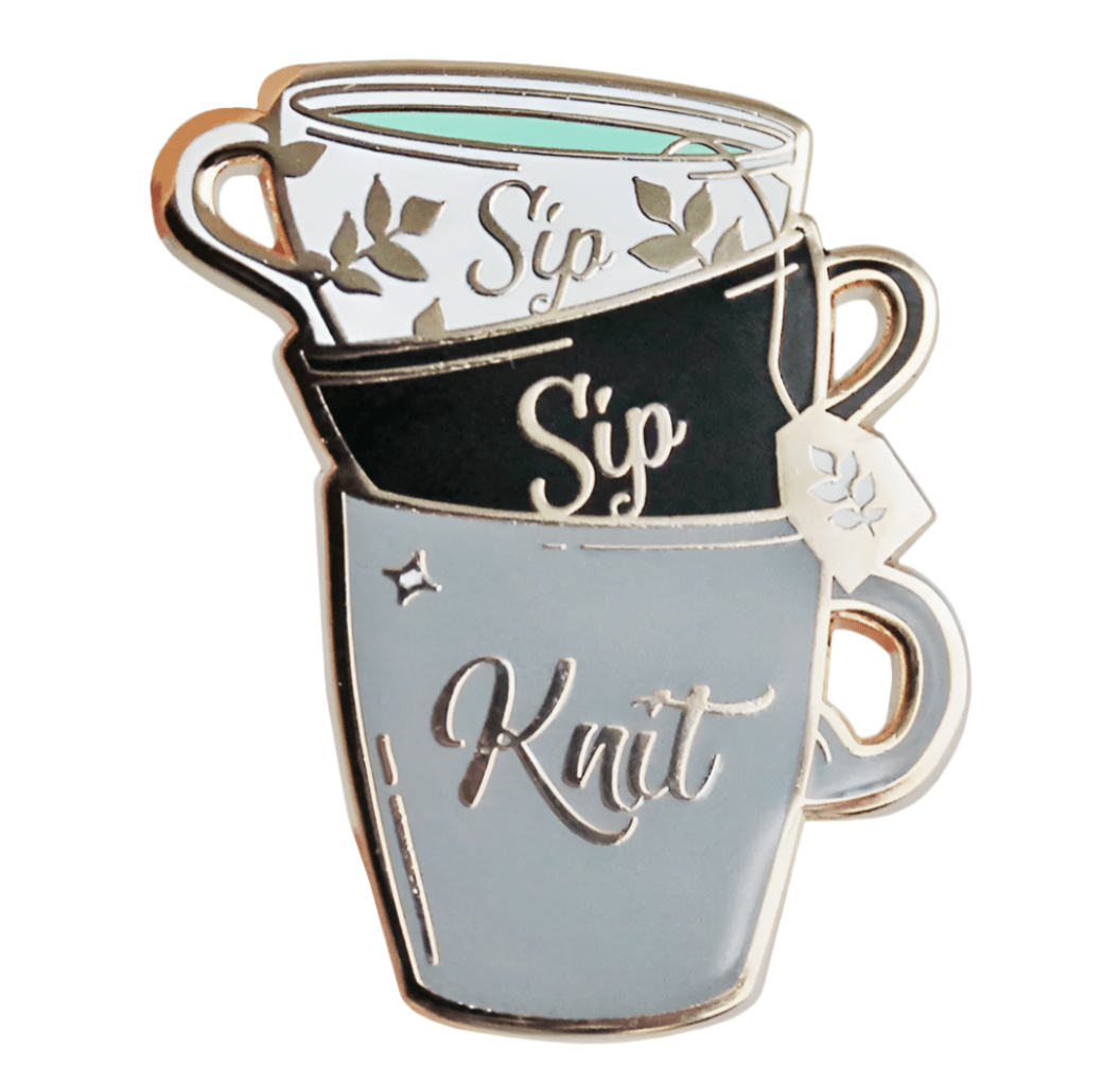 My Cutesy Era Black Sheep Club enamel pin features three stacked teacups accented with florals and a tea bag tag. The top two cups read Sip, the bottom Knit, all detailed in elegant black and gold.