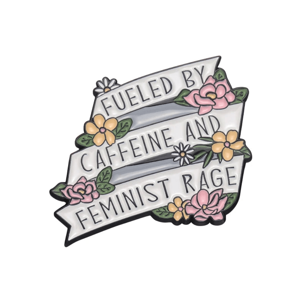 A 1-inch enamel pin by Kiss Me Later features a white ribbon reading Fueled by caffeine and feminist rage, accented with pink and yellow flowers, green leaves, and a reminder for more self love.