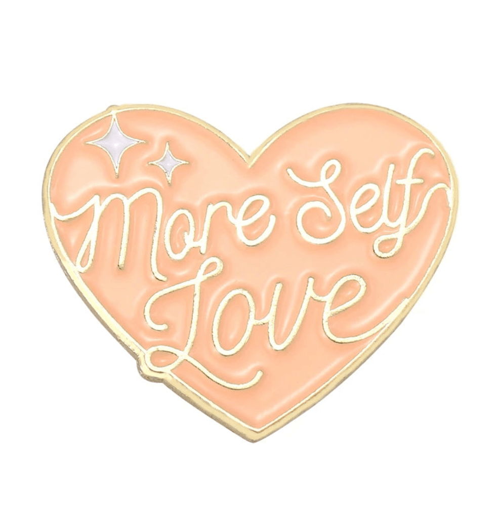 The Kiss Me Later 1 enamel pin features a peach heart with gold edges, More Self Love in cursive, and two white sparkles in the upper left corner.