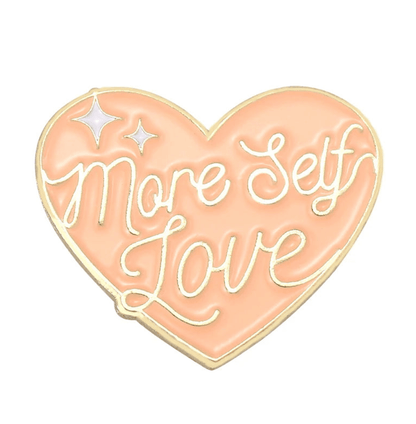 The Kiss Me Later 1 enamel pin features a peach heart with gold edges, More Self Love in cursive, and two white sparkles in the upper left corner.