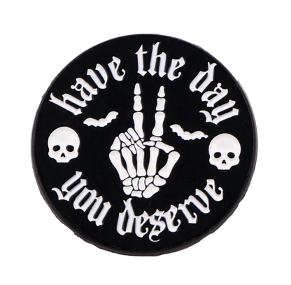 The Kiss Me Later round black skeleton pin features white “have the day you deserve” text, a peace sign skeleton hand, two skulls, and two bats—perfect for fans of gothic and emo pins.