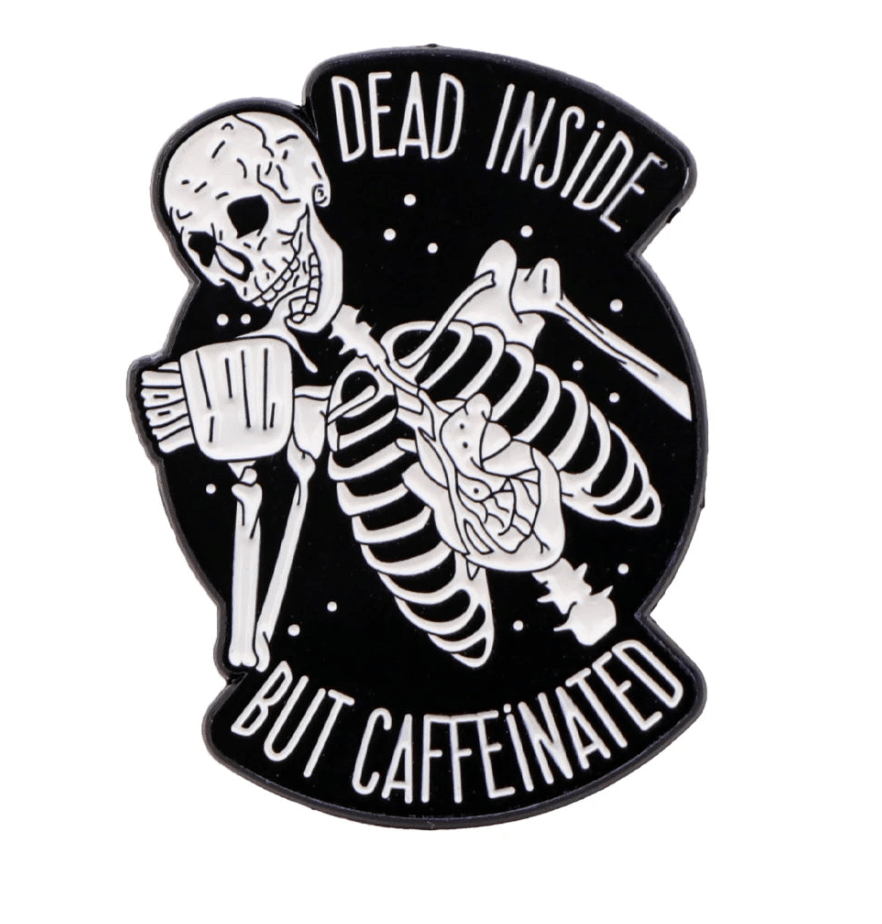 A black and white Kiss Me Later pin shows a grinning skeleton holding a coffee cup with “DEAD INSIDE BUT CAFFEINATED”—ideal for fans of gothic accessories and dark humor.