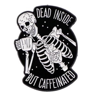 A black and white Kiss Me Later pin shows a grinning skeleton holding a coffee cup with “DEAD INSIDE BUT CAFFEINATED”—ideal for fans of gothic accessories and dark humor.