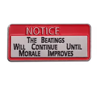 A Kiss Me Later enamel pin featuring a red border and bold text: NOTICE: THE BEATINGS WILL CONTINUE UNTIL MORALE IMPROVES. This rectangular pin is perfect for adding humor to your bag or jacket.
