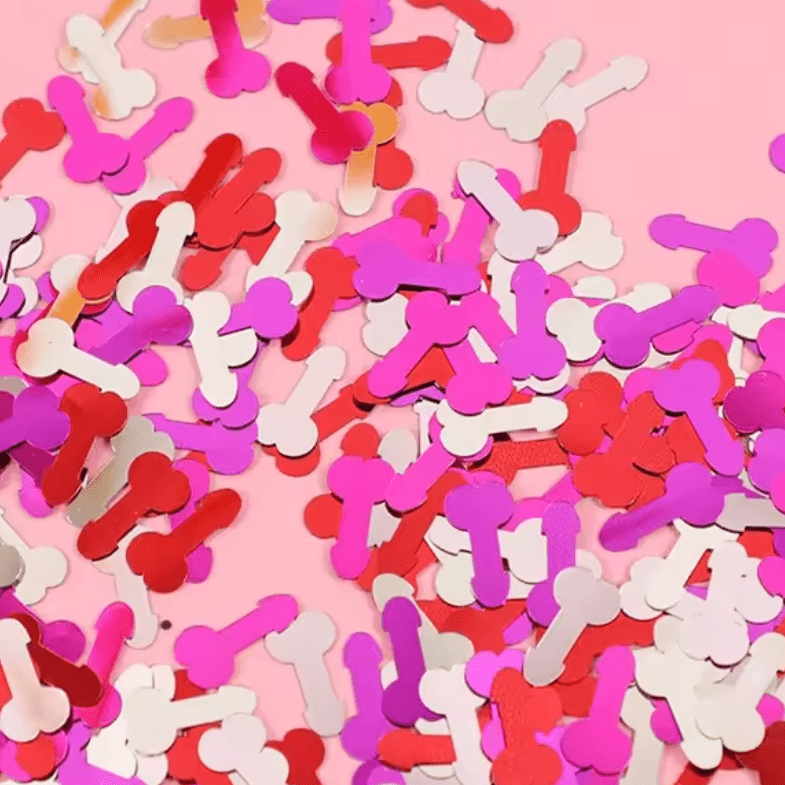 Kiss Me Later adult party confetti shaped like penises, in red, pink, and white, scattered on a pink background.
