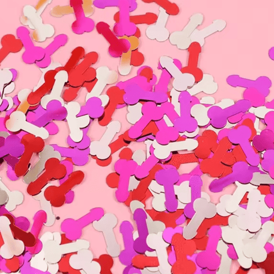 Kiss Me Later adult party confetti shaped like penises, in red, pink, and white, scattered on a pink background.