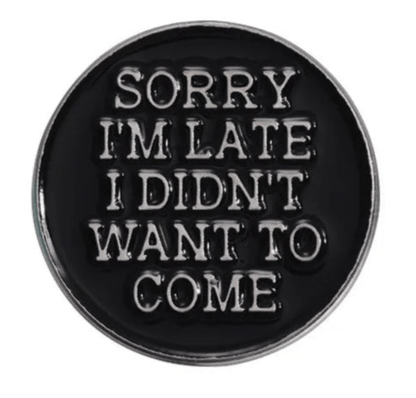 The Kiss Me Later round black enamel pin features raised silver letters that say, SORRY IM LATE I DIDNT WANT TO COME. This limited edition accessory makes a bold addition to any collection.
