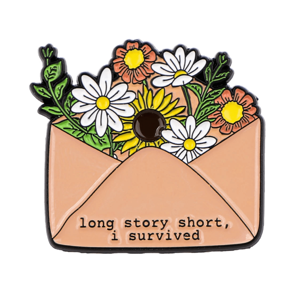 Kiss Me Later presents a motivational enamel pin: an open peach-colored envelope filled with colorful flowers, featuring the text, long story short, i survived.