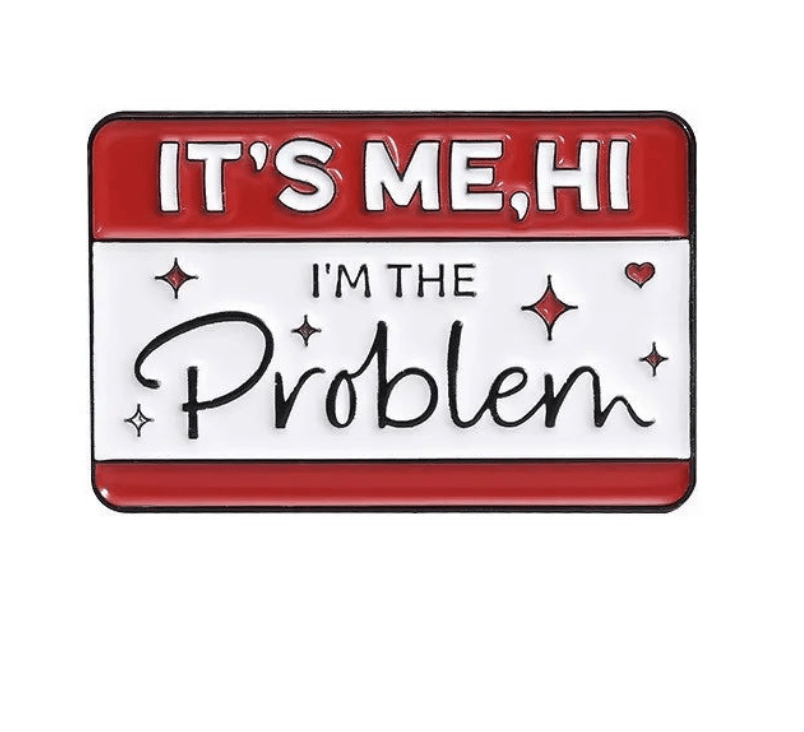 A rectangular enamel pin with a red and white background features the text ITS ME, HI IM THE Problem accented by small hearts and sparkles around Problem.