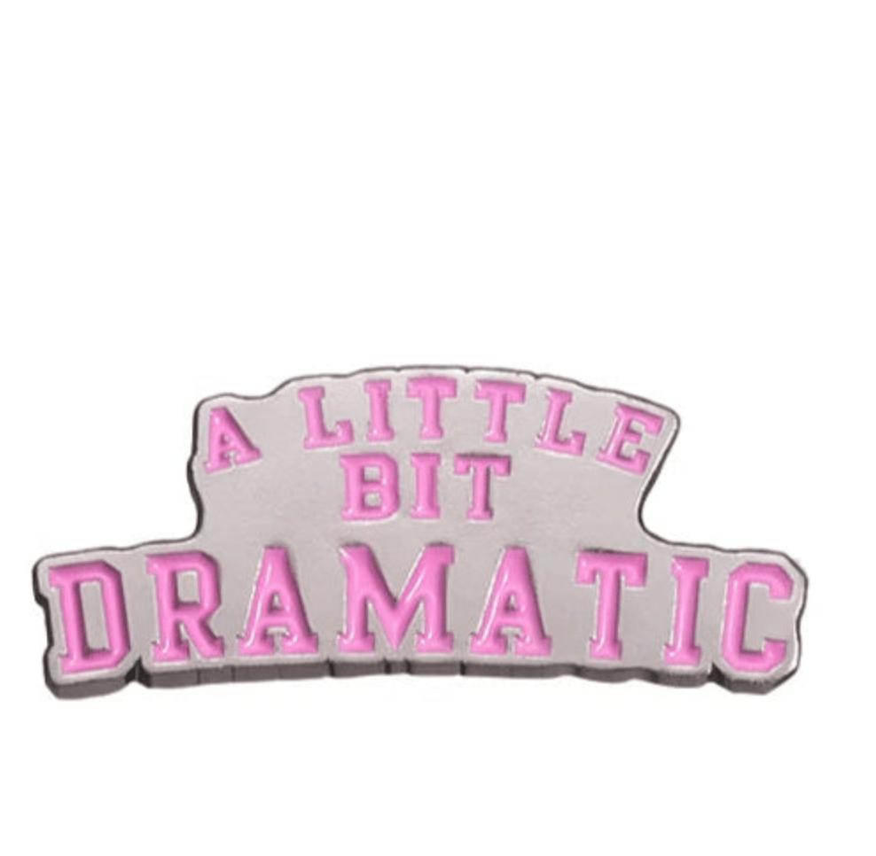 A Kiss Me Later enamel pin featuring A LITTLE BIT DRAMATIC in bold pink uppercase on light gray—ideal for empowered women and feminist pin fans.