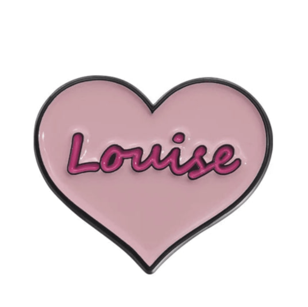 The Kiss Me Later enamel pin is pink and heart-shaped, featuring Louise in bold, cursive dark pink letters outlined in black—a perfect feminist accessory.