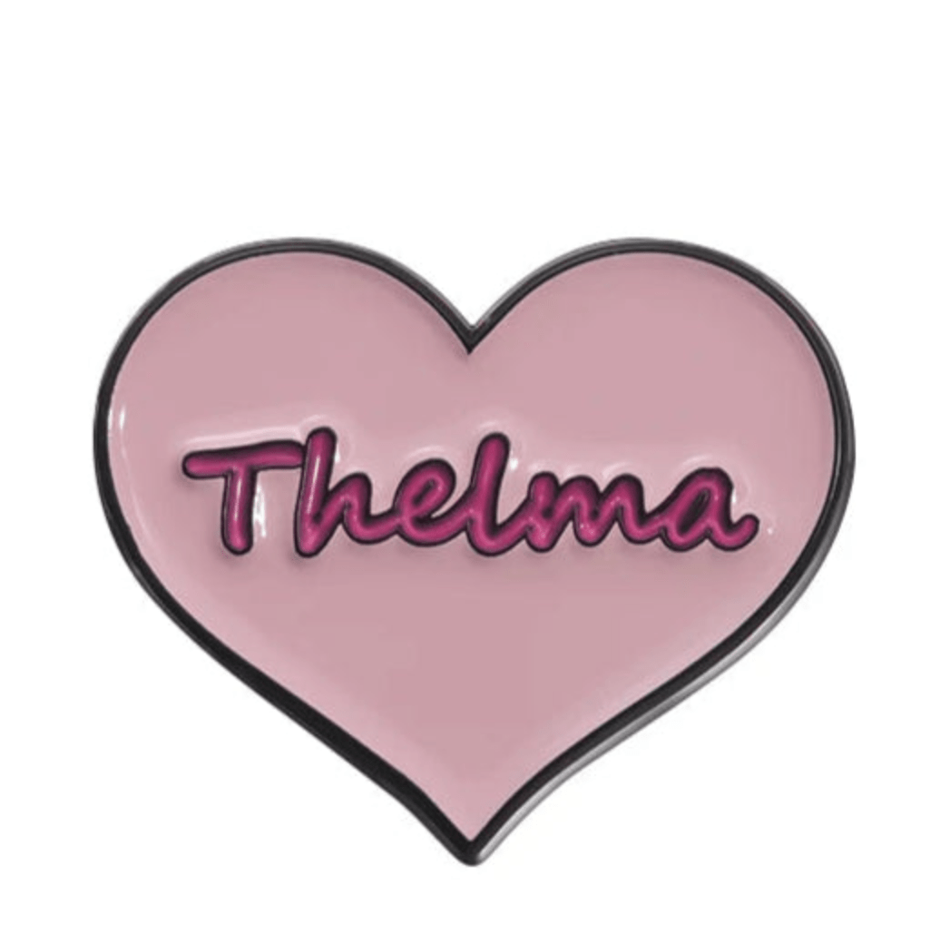 A pink, heart-shaped Kiss Me Later pin with Thelma in bold dark pink cursive—a charming enamel accessory for any feminist pin collection celebrating empowered women.
