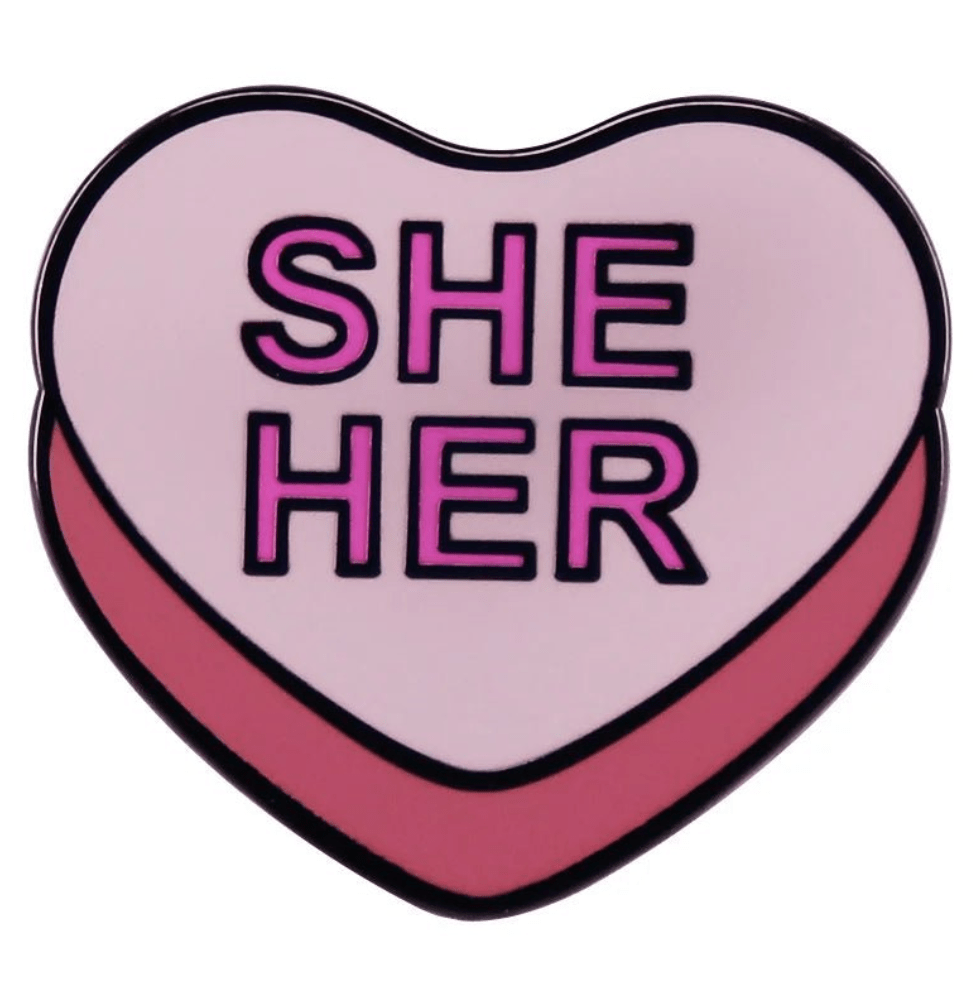 My Cutesy Era heart enamel pin features a light pink top, darker pink bottom, and bold SHE HER text in capital letters.