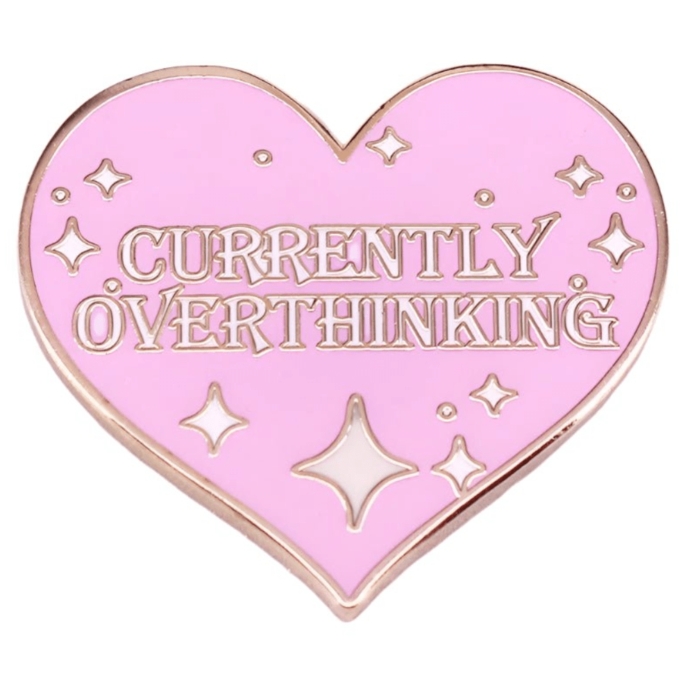 A pink heart enamel pin by My Cutesy Era features CURRENTLY OVERTHINKING in capitals, with small sparkle and star accents.