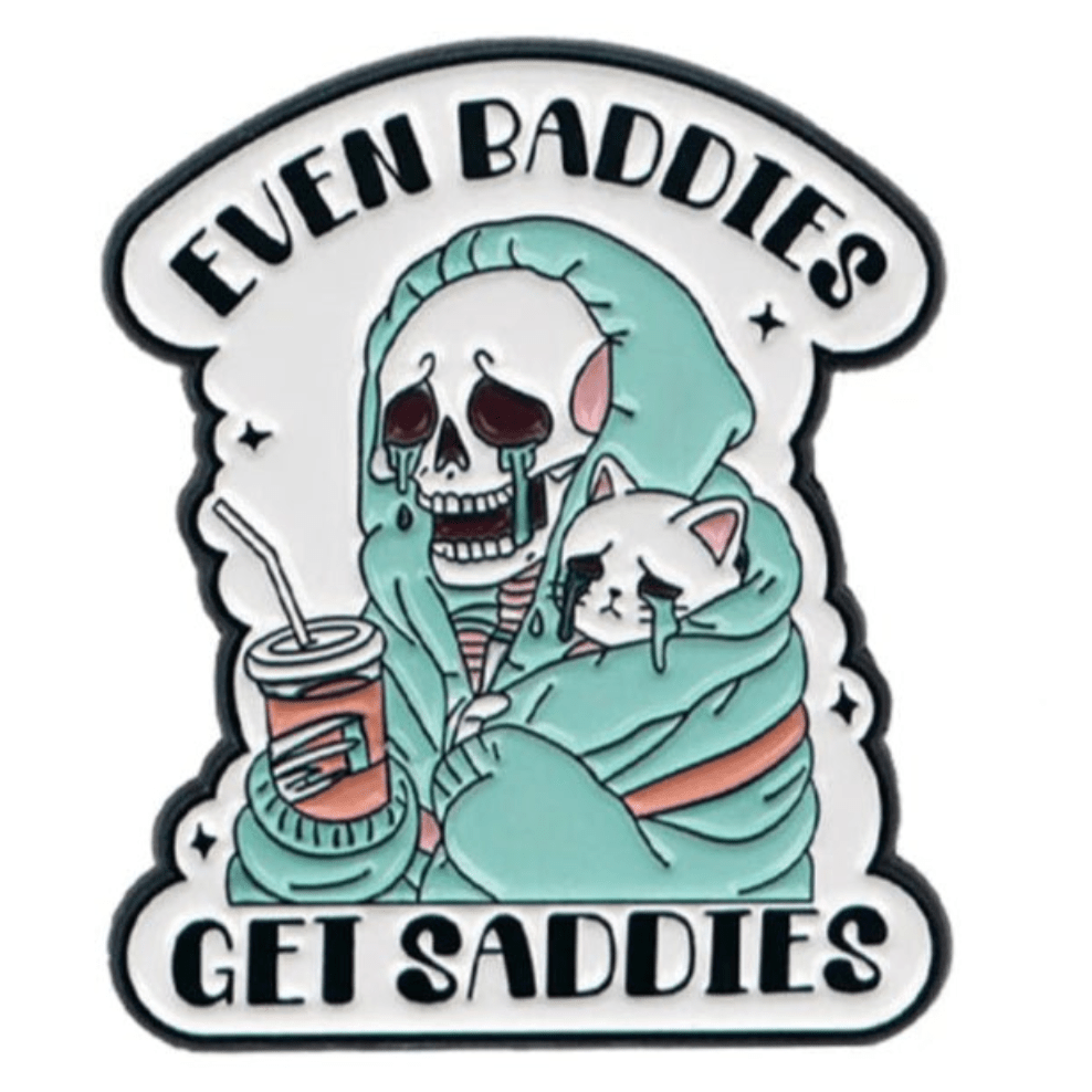 A skeleton in a hoodie hugs a cute cat pin and sips from a straw, tears streaming down. Text above and below reads Even baddies get saddies. By My Cutesy Era.