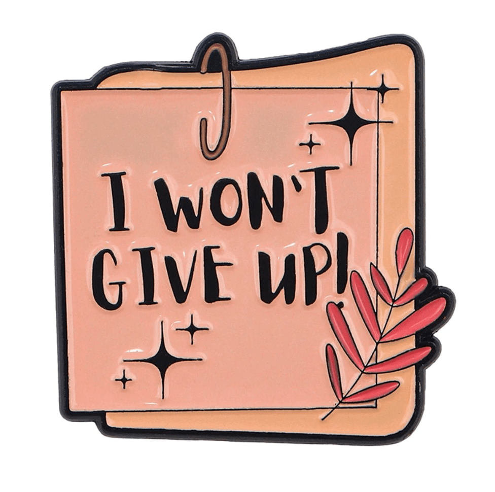 From My Cutesy Era, this pink enamel pin is shaped like a notepad with “I WONT GIVE UP!” in bold black letters, sparkles, and a pink leafy branch—perfect as a motivational mental health reminder or positive affirmation.