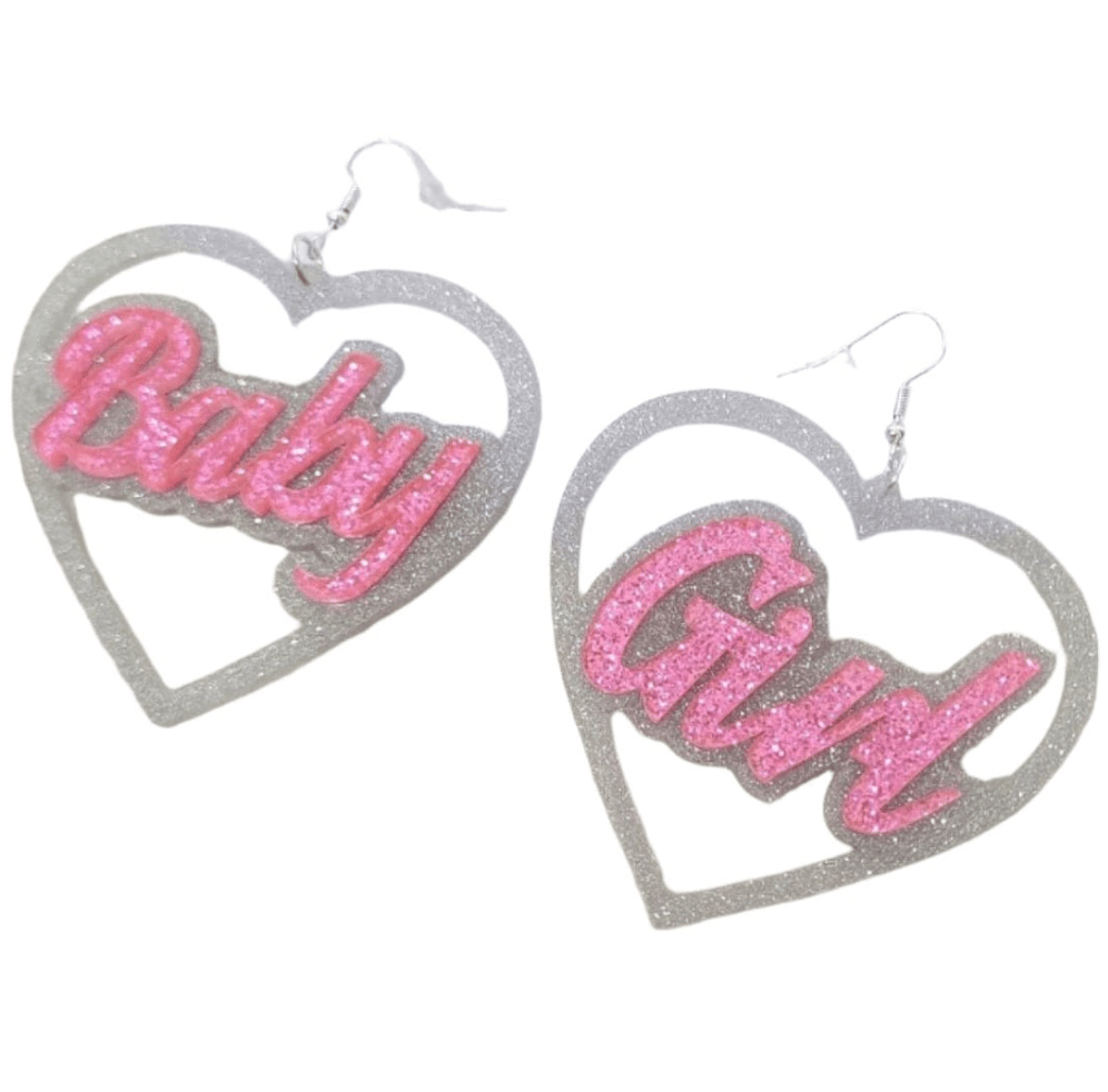 My Cutesy Era's love heart dangly earrings feature silver glitter outlines and pink glitter text—one says "Baby," the other "Girl." Sparkling statement BabyGirl earrings for a cute, eye-catching look.