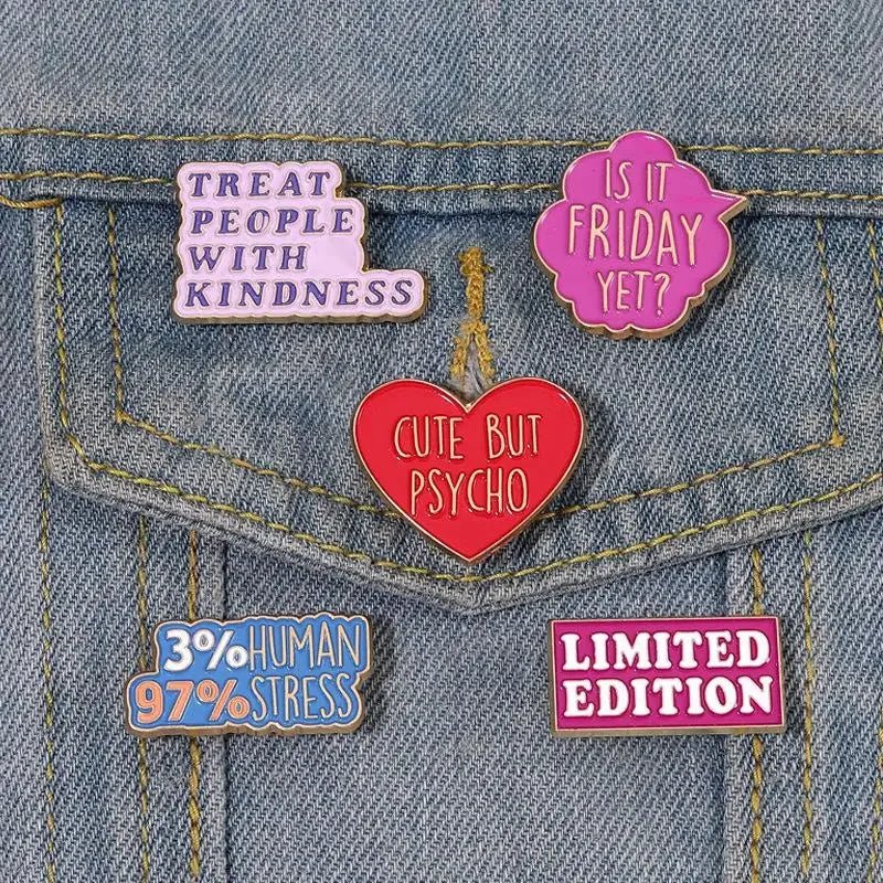 Five enamel pins including “Cute But Psycho” and a red love heart, are attached to blue denim. Pins read: TREAT PEOPLE WITH KINDNESS, IS IT FRIDAY YET?, 3% HUMAN 97% STRESS, and LIMITED EDITION.