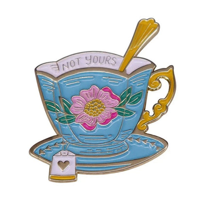 My Cutesy Era's enamel pin features a blue floral tea cup with a pink flower, gold handle and saucer, spoon inside, tea bag on the plate, and NOT YOURS in bold on the rim.