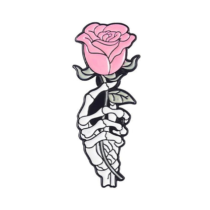 A stylized drawing of a skeletal hand clutching a pink rose with green leaves on a white background, inspired by the edgy style seen in skull enamel pins.
