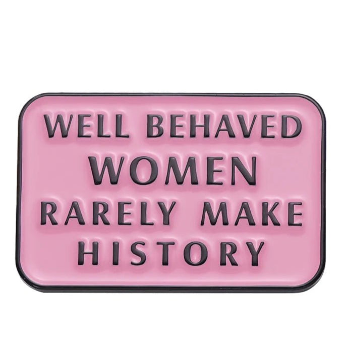 A rectangular pink enamel pin with raised black letters reading WELL BEHAVED WOMEN RARELY MAKE HISTORY—a bold accessory for self-love and empowerment.