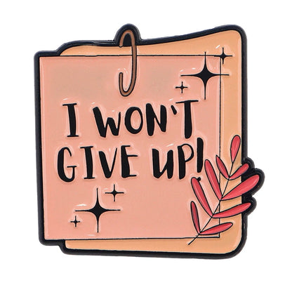Pin shaped like a sticky note with I WONT GIVE UP! in bold black letters, sparkles, and a red leaf—an inspiring accessory for self-empowerment and positive mental health affirmations.