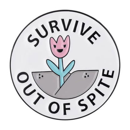 A  round enamel pin shows a smiling pink flower sprouting from a gray crack, with SURVIVE OUT OF SPITE in bold black letters on white. An inspiring accessory for anyone who perseveres against the odds.