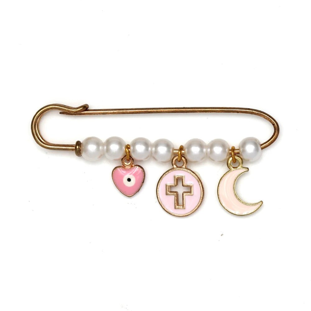 The Kiss Me Later gold safety pin brooch features five white pearls and three dangling charms—a pink heart with black dot, a pink circle with gold cross, and a cream crescent moon—making it a unique baby shower gift.