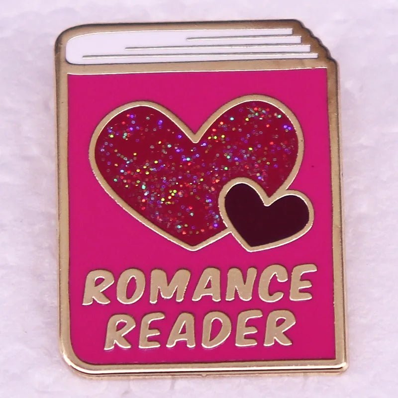 Pink enamel pin, shaped like a book with glittery red hearts and ROMANCE READER in gold, is perfect for enamel pin collectors and book lovers looking for a unique badge.
