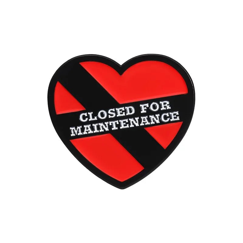 Enamel pin features a red heart with a bold black “X” and white text in the center that says “CLOSED FOR MAINTENANCE.”.