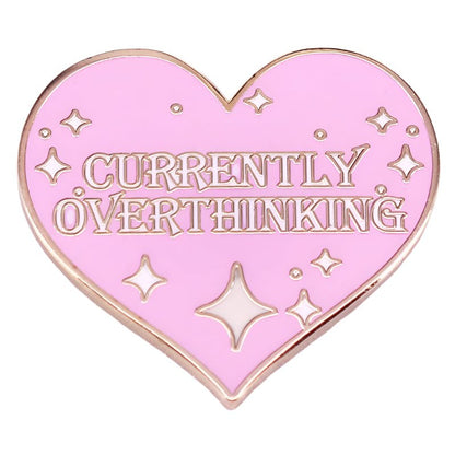 The My Cutesy Era enamel pin is heart-shaped and pink with gold trim and sparkles, featuring CURRENTLY OVERTHINKING in bold gold letters.
