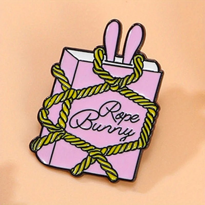 Pnk rectangular enamel pin features two bunny ears at the top, yellow rope details, and “Rope Bunny” in cursive on a soft peach background