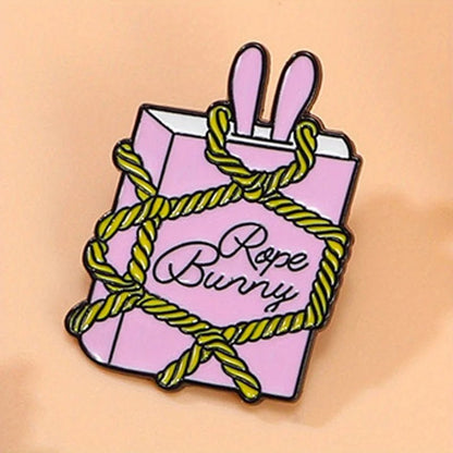 Pnk rectangular enamel pin features two bunny ears at the top, yellow rope details, and “Rope Bunny” in cursive on a soft peach background