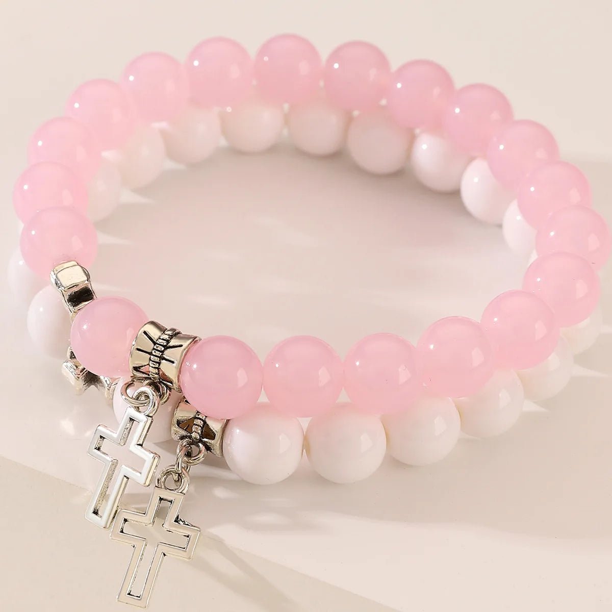 Stacked together, these Kiss Me Later beaded stretch bracelets feature light pink and white crystal beads, each adorned with a delicate silver cross charm for a stylish touch of faith.